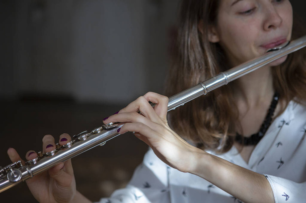 A beautiful woman posing while playing on a flute Flute in hands of girl during the concert. Genre portrait of young beautiful girlr Close-up - 写真・画像