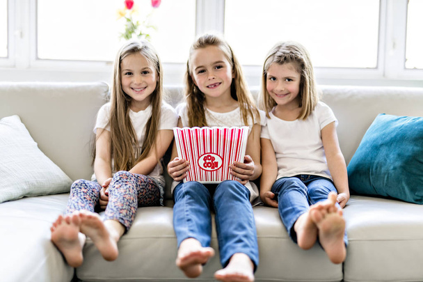 happy little girls watching comedy movie on tv and eating popcorn at home - Fotó, kép