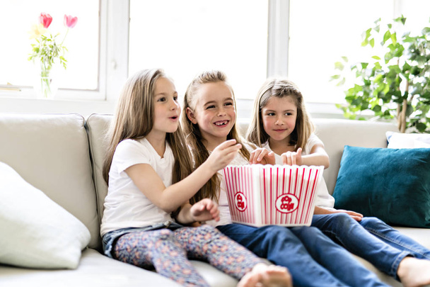happy little girls watching comedy movie on tv and eating popcorn at home - Photo, image