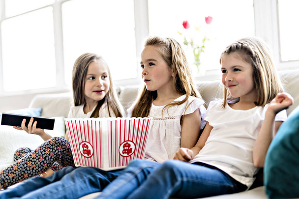 happy little girls watching comedy movie on tv and eating popcorn at home - Foto, immagini