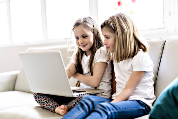 Happy little girls at home working with a laptop on sofa - Foto, Imagem