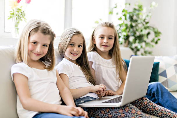 Happy little girls at home working with a laptop on sofa - Foto, Imagen