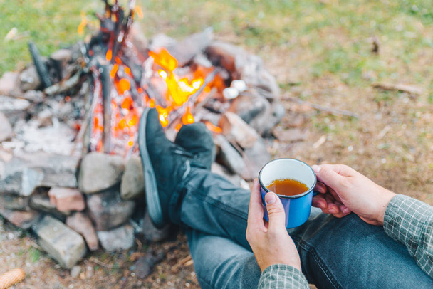 最初のビュー ポイント。キャンプの火の近くの金属のカップでお茶を飲む男。ハイキング - 写真・画像