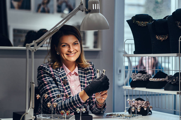 Жінка-працівник ювелірних виробів, що показує красиві дорогоцінні сережки з дорогоцінними каменями в розкішному магазині ювелірних виробів
. - Фото, зображення