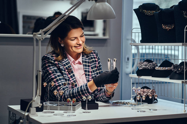Trabalhadora de jóias feminina mostrando belos brincos preciosos com pedras preciosas em uma joalharia de luxo
. - Foto, Imagem