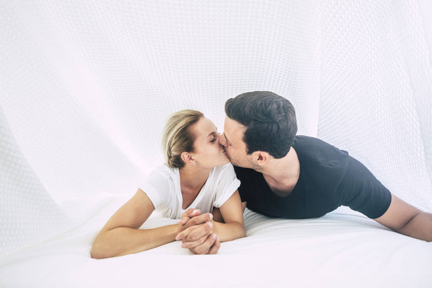 Nuori pari makaa ja suutelee sängyssä makuuhuoneessa
 - Valokuva, kuva