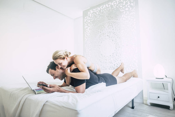 young couple laying on bed and working on laptop in bedroom - Fotó, kép