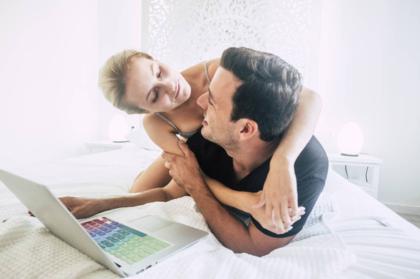 jeune couple couché sur le lit et travaillant sur ordinateur portable dans la chambre
 - Photo, image