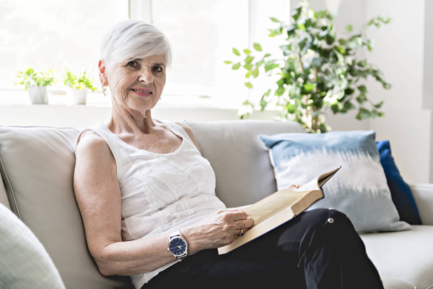 Senior woman reading book at home by fireplace - Foto, Bild
