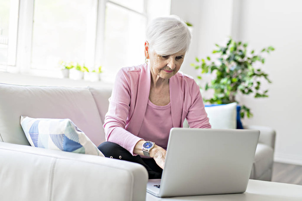 Retired senior woman sitting at home using her laptop - Photo, Image