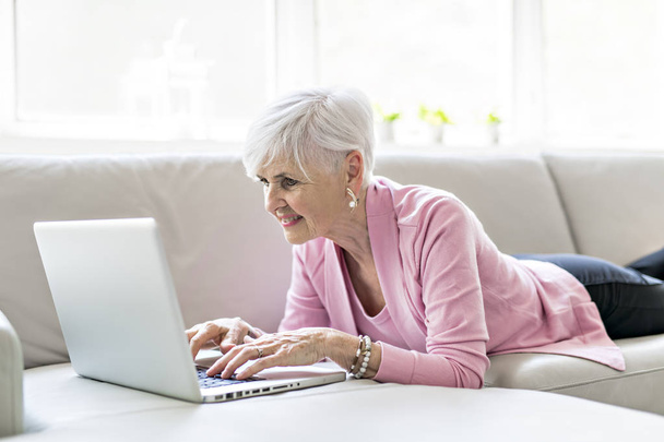 Retired senior woman sitting at home using her laptop - Фото, изображение