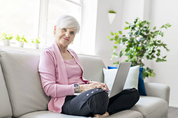 Retired senior woman sitting at home using her laptop - Foto, afbeelding