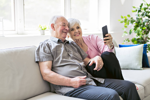 Affectionate attractive elderly couple sitting together on a couch taking selfie - Photo, image