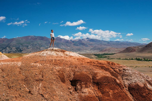 Girl tourist stands on the top of the mountain. Tourist on a high red hill. Landscape and travel to the mountains - Foto, imagen