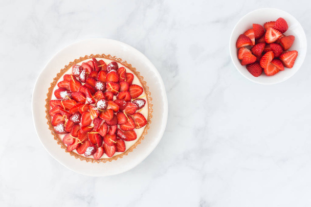 Homemade strawberry cake with lemon cream and a bowl of cut strawberries on white marble with copy space. - Photo, Image