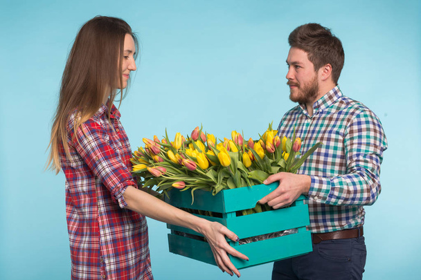 Gelukkig man en vrouw bloemisten houden doos met tulpen en lachen op blauwe achtergrond - Foto, afbeelding