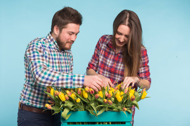 Lale kutusuyla tutarak ve mavi zemin üzerine gülen mutlu erkek ve kadın çiçekçi - Fotoğraf, Görsel