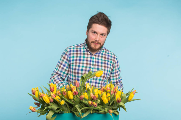 Kwiaciarnia wesoły przystojny mężczyzna z pola tulipanów na niebieskim tle - Zdjęcie, obraz