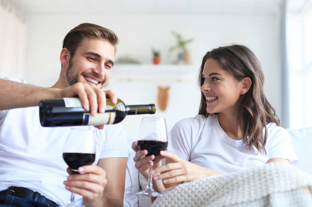Jovem casal amoroso bebendo um copo de vinho tinto em sua sala de estar. - Foto, Imagem