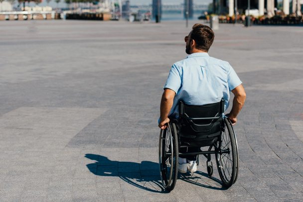 back view of man in sunglasses using wheelchair on street - Foto, imagen