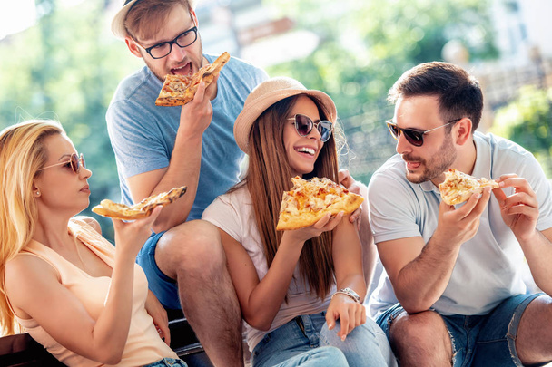 Ryhmä iloisia ystäviä syö pizzaa puistossa
 - Valokuva, kuva