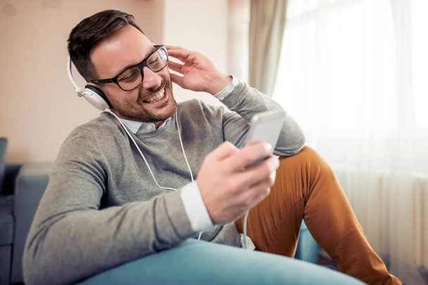 Young man listening to music on his smart phone at home. - Foto, Imagen