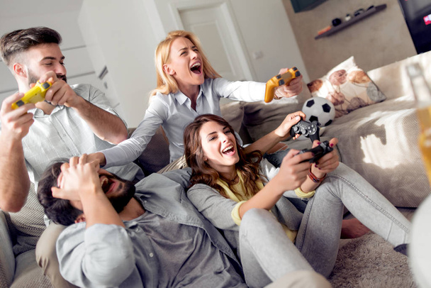 Ομάδα νέων φίλων κάθεται σε μοντέρνο διαμέρισμα και βιντεοπαιχνίδια. Έννοια της φιλίας, της τεχνολογίας, παιχνίδια και σπίτι. - Φωτογραφία, εικόνα