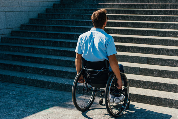 вид ззаду людини, що використовує інвалідне крісло на вулиці і дивиться на сходи без пандуса
 - Фото, зображення
