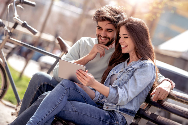 Jeune couple assis dans le banc du parc et s'amuser avec une tablette
 - Photo, image