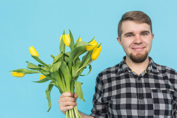Человек с букетом желтых тюльпанов. Желтые тюльпаны в руках бородатого человека на синем фоне
 - Фото, изображение