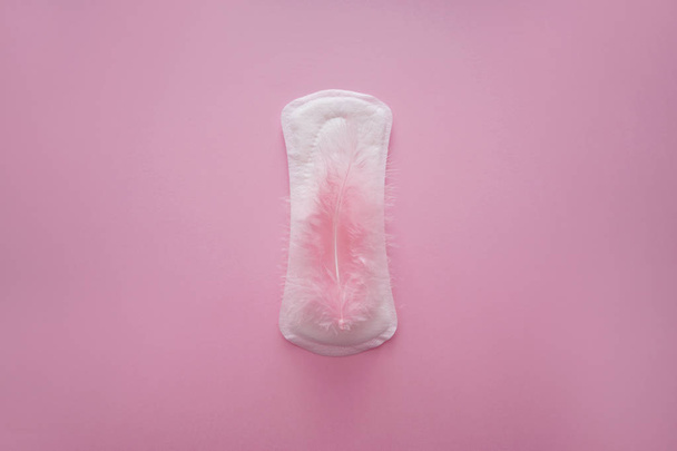 Menstrual pad with feather on color background - Фото, изображение