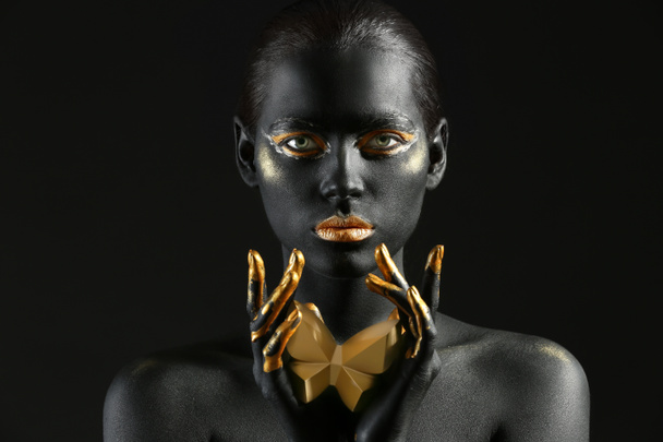 Belle femme avec de la peinture noire et dorée sur son corps sur fond sombre - Photo, image