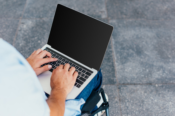 cropped image of man in wheelchair using laptop with blank screen on street - Photo, Image