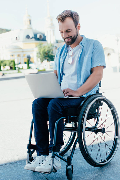 knappe man in rolstoel met behulp van laptop op straat - Foto, afbeelding