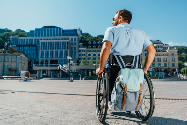 πίσω όψη του ανθρώπου που χρησιμοποιούν αναπηρικό αμαξίδιο με την τσάντα στον δρόμο - Φωτογραφία, εικόνα