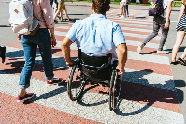back view of boyfriend in wheelchair and girlfriend crossing crosswalk in city - Photo, Image