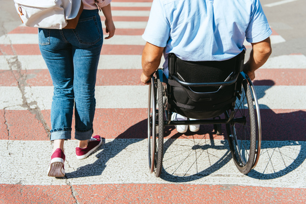 cropped image of boyfriend in wheelchair and girlfriend crossing crosswalk in city - Fotó, kép