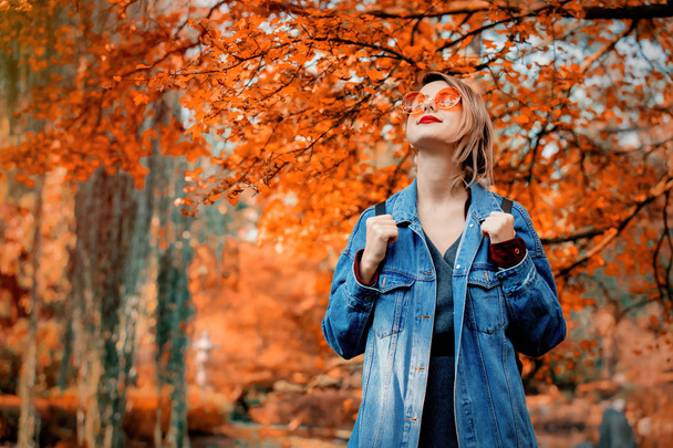 公園で眼鏡と青のデニム ジャケットでスタイリッシュな女性。秋シーズンの時間 - 写真・画像