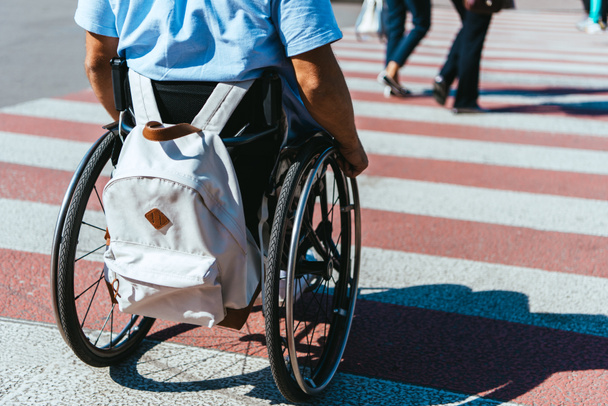 cropped image of man in wheelchair with bag riding on crosswalk - Фото, зображення
