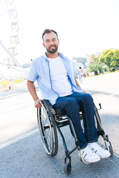 hymyilevä komea mies käyttää pyörätuolia kadulla ja katsot kameraa
 - Valokuva, kuva