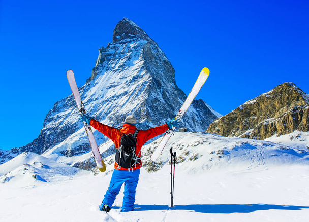Людина на лижах на снігу свіжого порошку. У зимовий сезон, гори і лижного туризму беккантрі обладнання на вершині засніжених гір на лижах в сонячний день з гори Маттерхорн у фоновому режимі, Церматт в швейцарських Альпах. - Фото, зображення