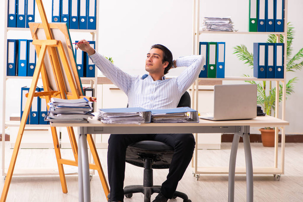 Jonge knappe werknemer geniet van het schilderen op kantoor  - Foto, afbeelding