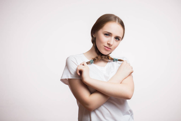 Funny young beautiful woman closed her braid and looks at the camera on a white background with copy space for text. Student or teen girl wearing white t-shirt - Foto, Bild