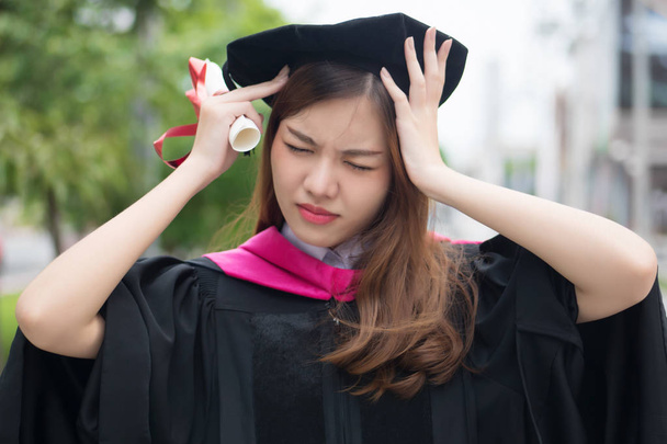 unglückliche, gestresste Studentin mit Hochschulabschluss; Porträt einer Diplom- oder Hochschulstudentin mit Hochschulabschluss mit Kopfschmerzstress, hartes Ausbildungskonzept; asiatisches Modell für junge erwachsene Frauen - Foto, Bild
