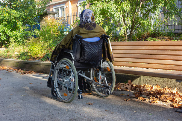 senior lady with a wheel chair on a sunny fall evening shining warm light through tree at city park - Foto, Imagen