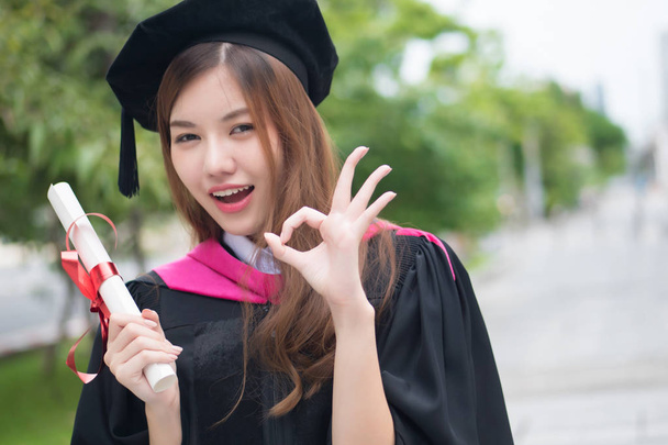 happy smiling graduated woman university student points ok sign; portrait of smiling woman student with graduation diploma or college degree giving ok hand gesture; asian 20s young adult woman model - Photo, Image