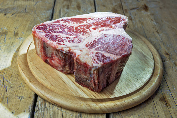 Placa de corte de madeira redonda com carne de porco crua na mesa de madeira
 - Foto, Imagem