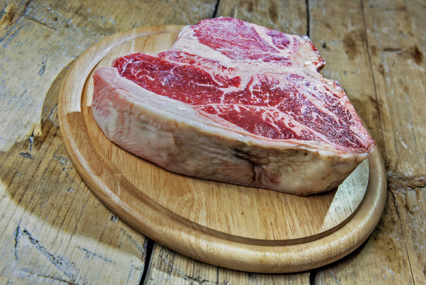 Round wooden chopping board with raw porterhouse beef on wooden table - Photo, Image