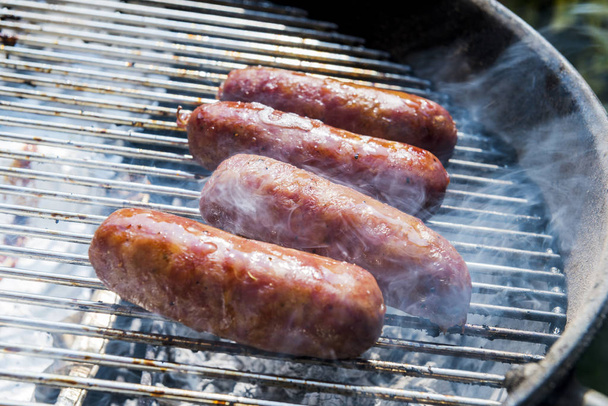 Four Sausages cook on the grill of barbecue - Fotó, kép