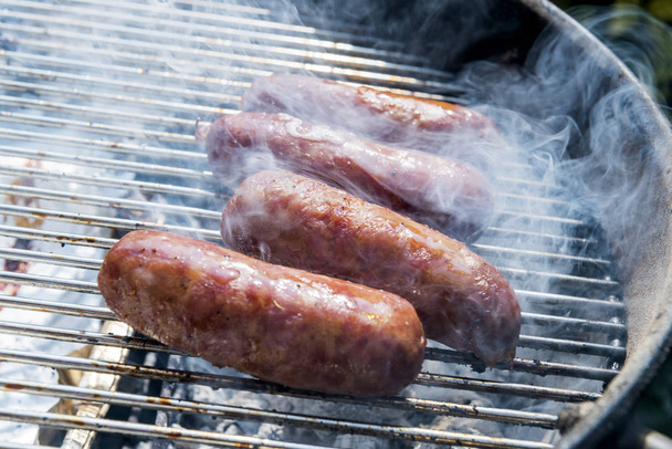 Quatre saucisses cuisent sur le gril du barbecue
 - Photo, image
